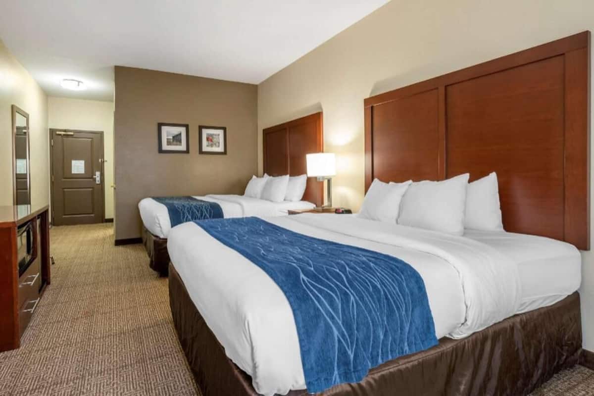 A hotel room with two beds, a desk, and a lamp.