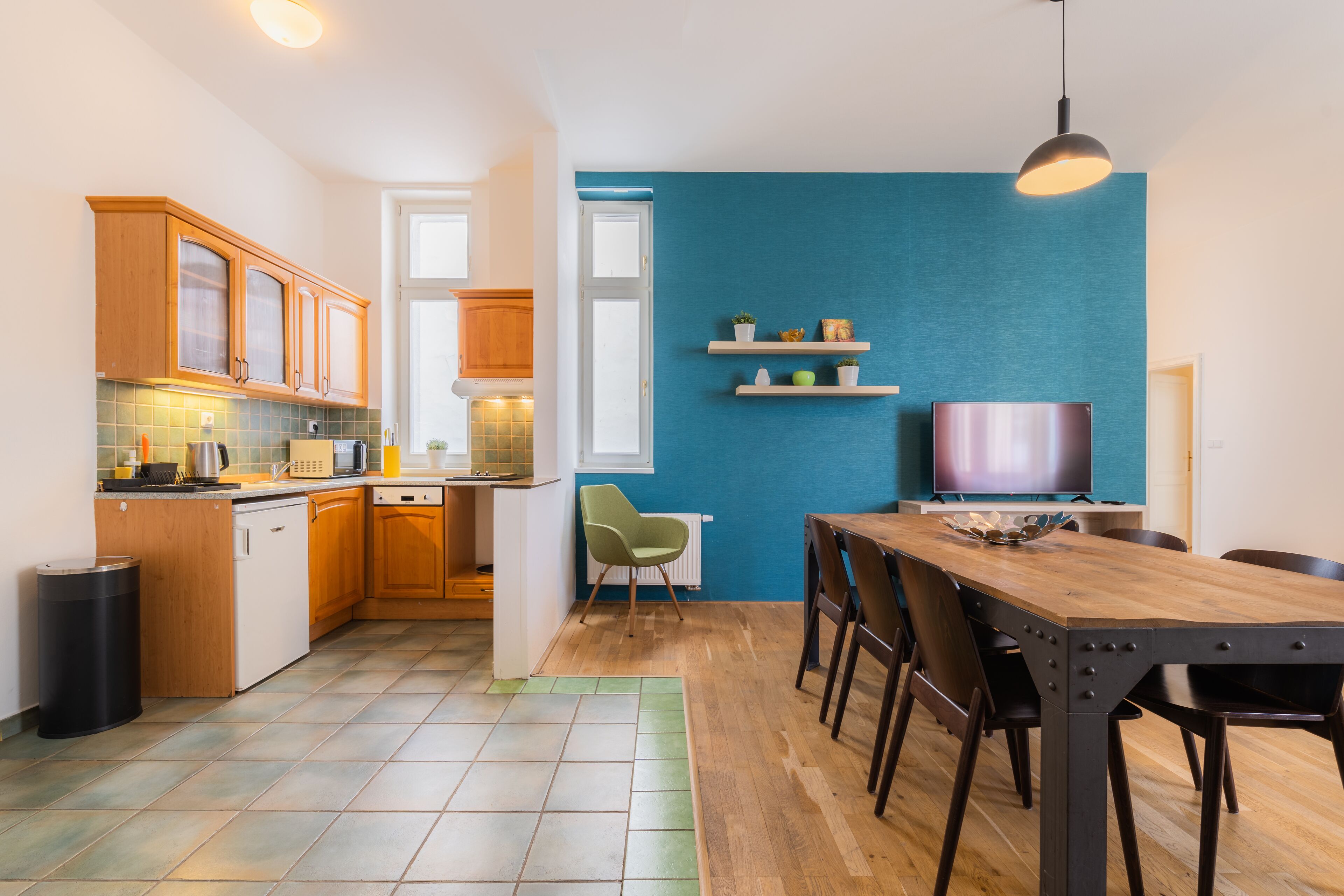 Une cuisine moderne avec des meubles en bois, un coin repas avec une table et des chaises en bois, et un mur d’accent bleu.