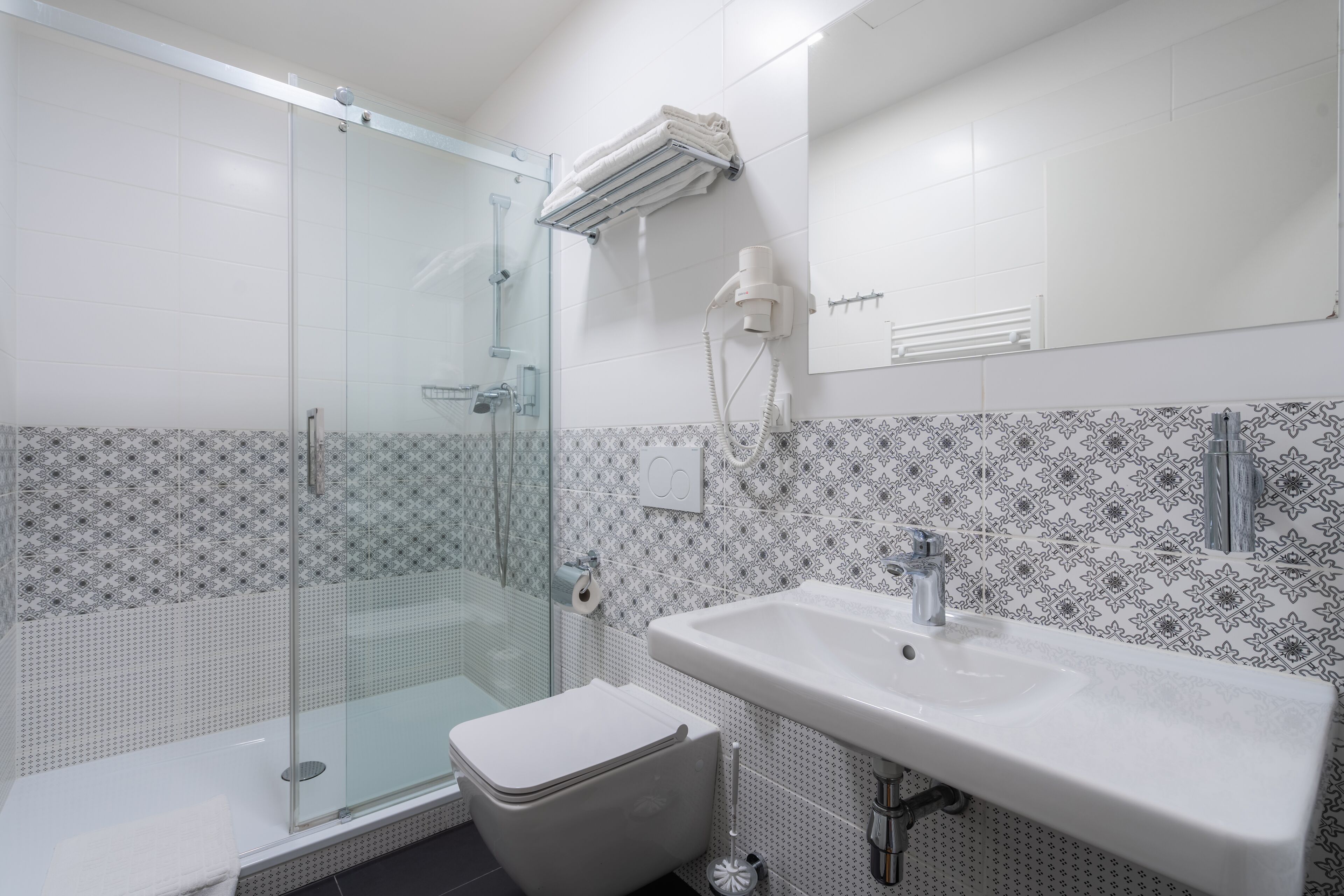 Ein modernes Badezimmer mit einer Duschkabine aus Glas, einem weißen Waschbecken und fliesenbesetztem Boden.