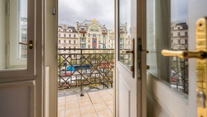 A view from a balcony with a metal railing, overlooking a street with buildings and parked cars.