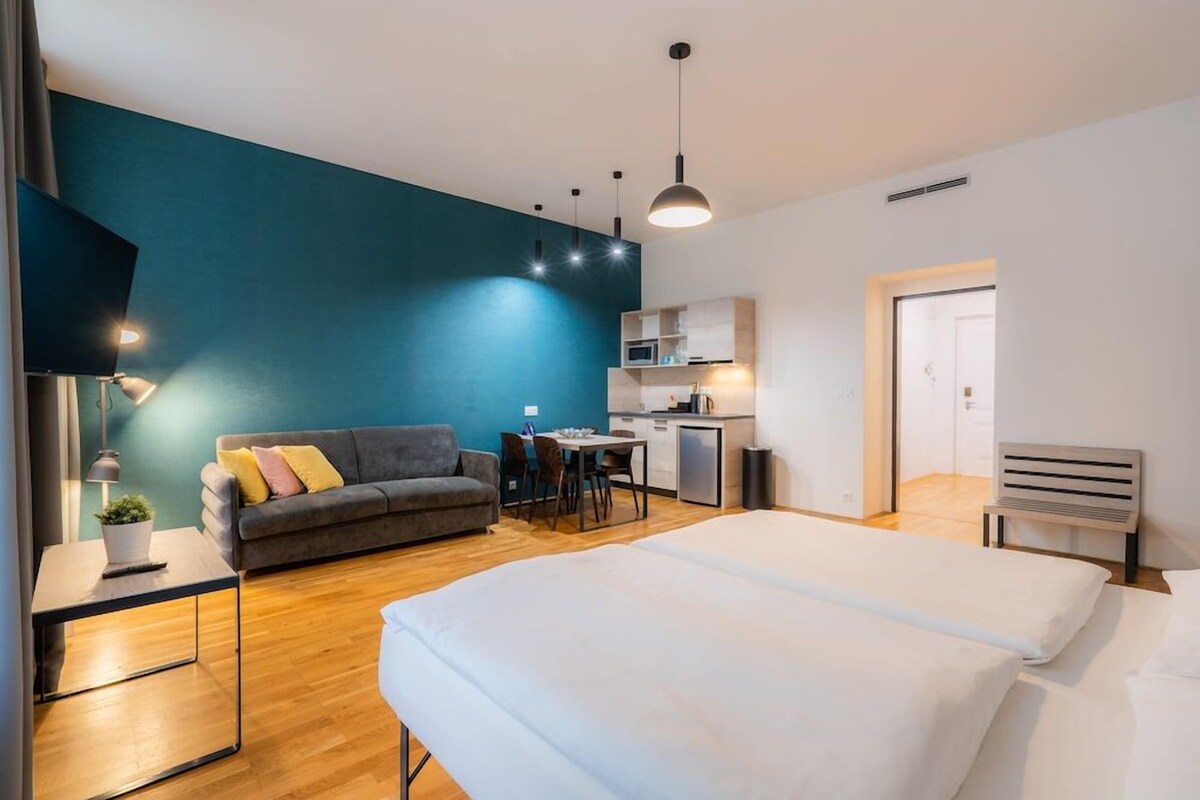 Un dormitorio moderno con una cama grande, un sofá, un escritorio y una kitchenette.