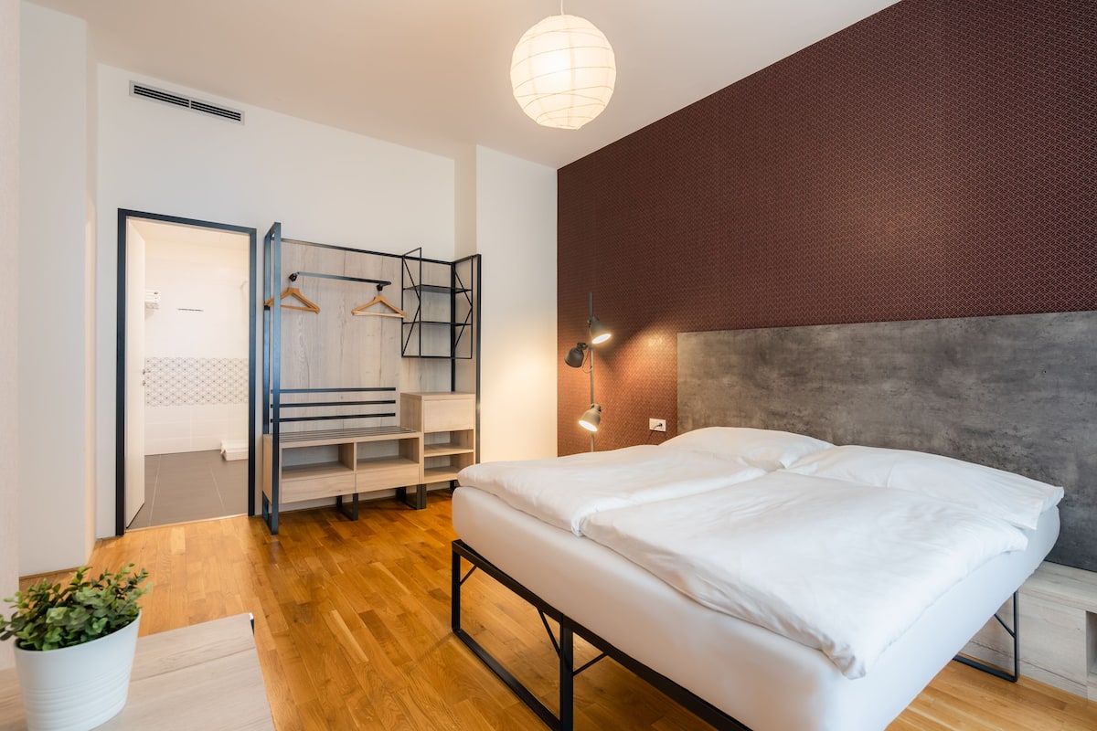 Une chambre à coucher moderne avec un lit, un plancher en bois, une armoire, un portant et un luminaire suspendu.