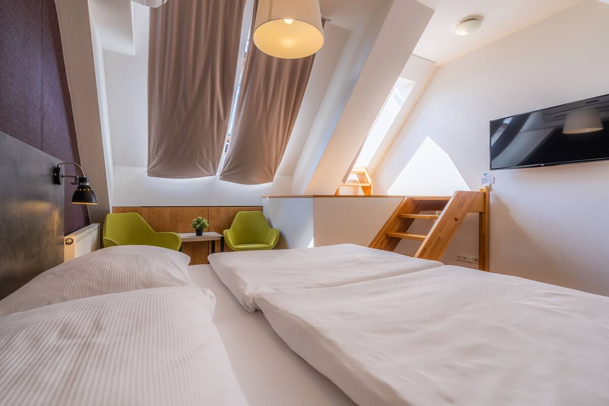 Une chambre d’hôtel moderne avec un lit en mezzanine, un bureau, une chaise et un téléviseur fixé au mur.