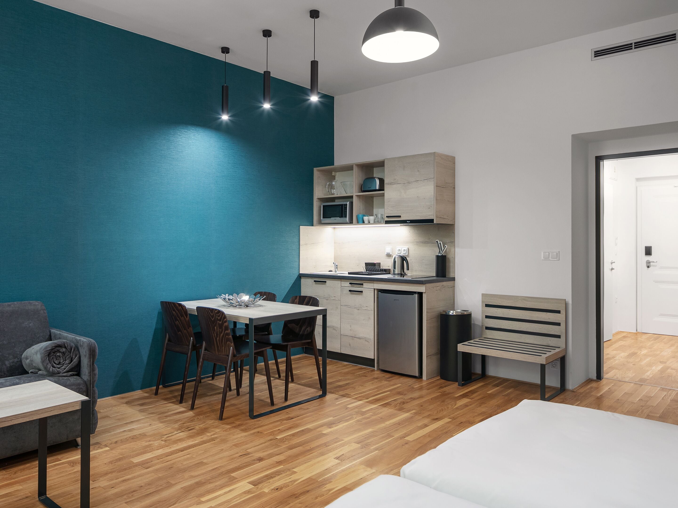 A modern room with a dining table, chairs, a sofa, a bench, and a kitchenette.