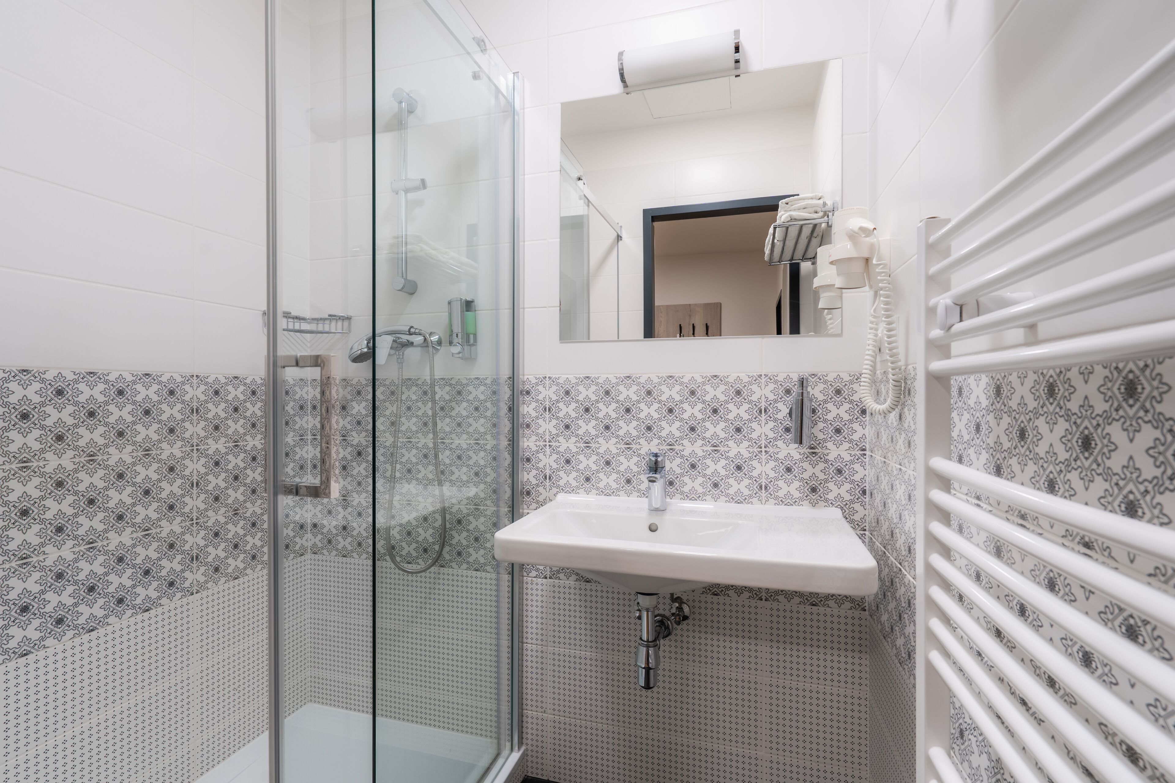 A bathroom with a glass shower enclosure, a white sink, and patterned tiles.