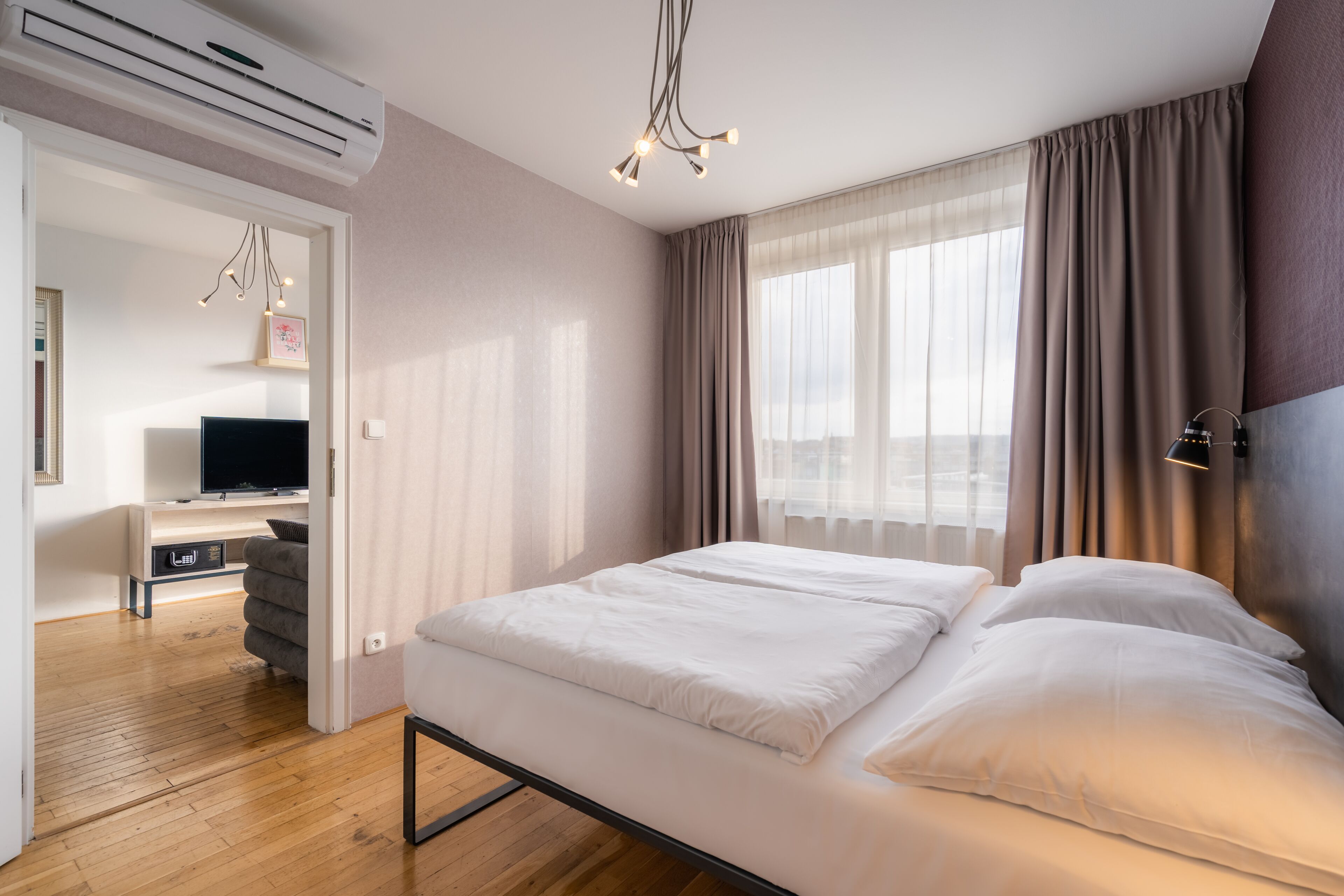 Una habitación de hotel con cama, escritorio con televisor y ventana con cortinas.