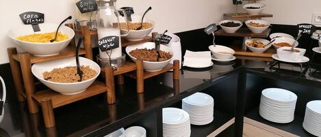 A buffet with labeled bowls of various breakfast items like cereal, yogurt, and granola.