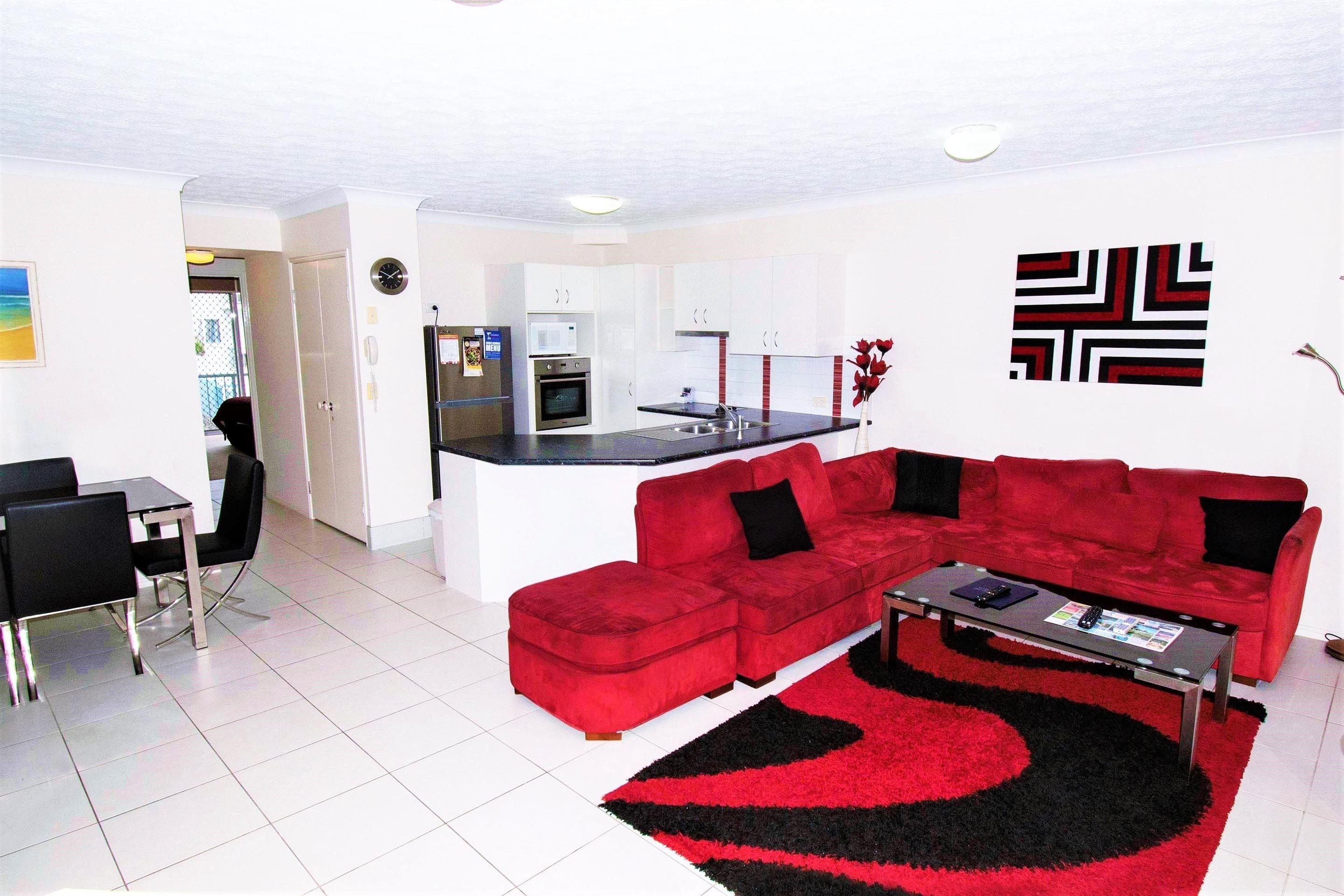 A modern living room with a red sectional sofa, a coffee table, and a kitchen in the background.