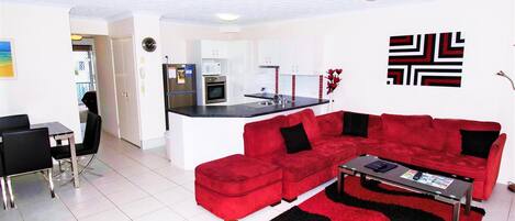 A modern living room with a red sectional sofa, a coffee table, and a kitchen in the background.