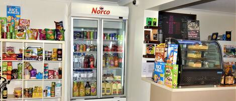 A convenience store with a refrigerated section labeled 'Norco', shelves stocked with snacks, beverages, and a coffee bar.
