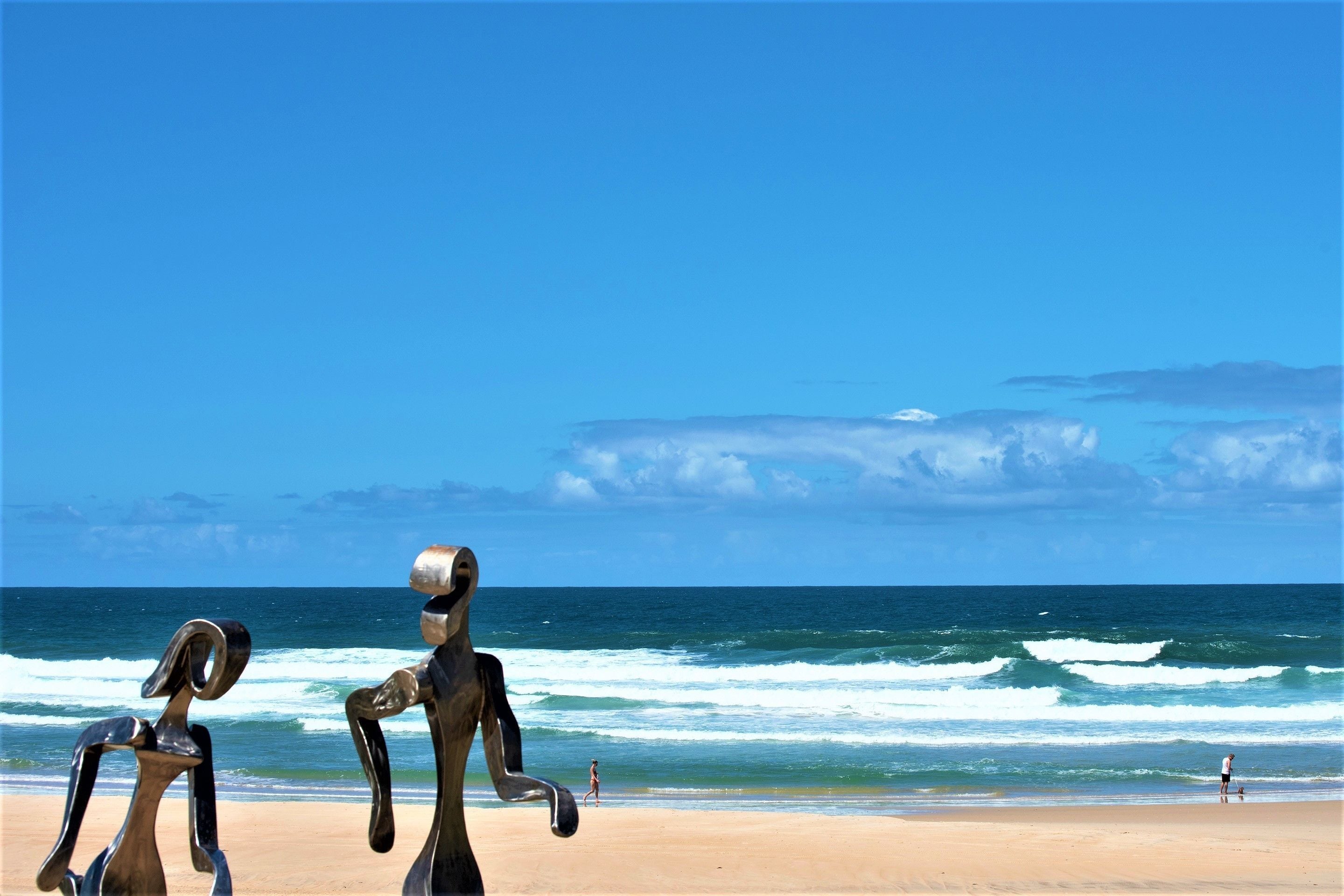 A beach with two metallic sculptures and a clear blue sky.