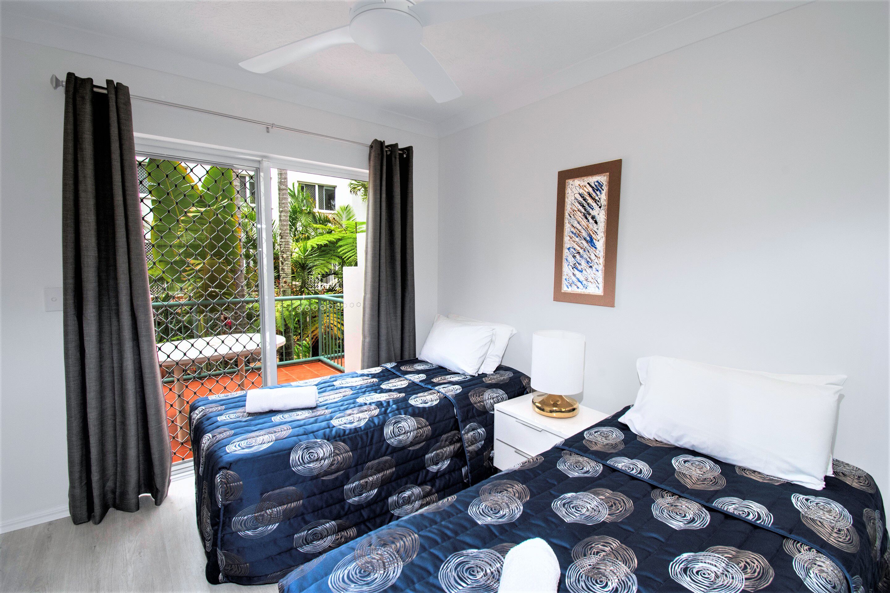 A hotel room with two beds, a balcony, and a ceiling fan.