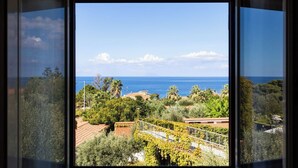 A coastal view through a window, featuring a clear sky, ocean, and lush greenery. - Tonicello Resort & SPA (Ricadi)