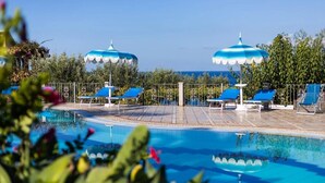 A pool area with lounge chairs and umbrellas, surrounded by greenery and a clear sky. - Tonicello Resort & SPA (Ricadi)