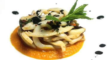 Eine Portion Pasta mit grünen Blättern und einem Soßenüberzug.
