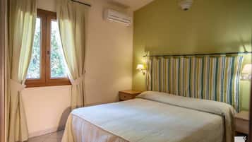A bedroom with a bed, an air conditioner, a window with curtains, a bedside lamp, and a radiator.