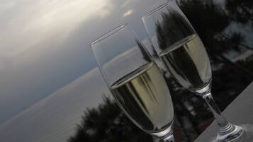 Dos copas de champán en un balcón con vista al mar y árboles al fondo.