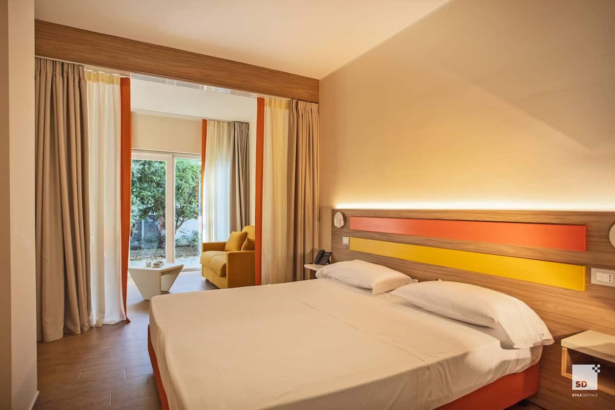 A hotel room with a large bed, a bedside table, a chair, and a view of the outdoors.