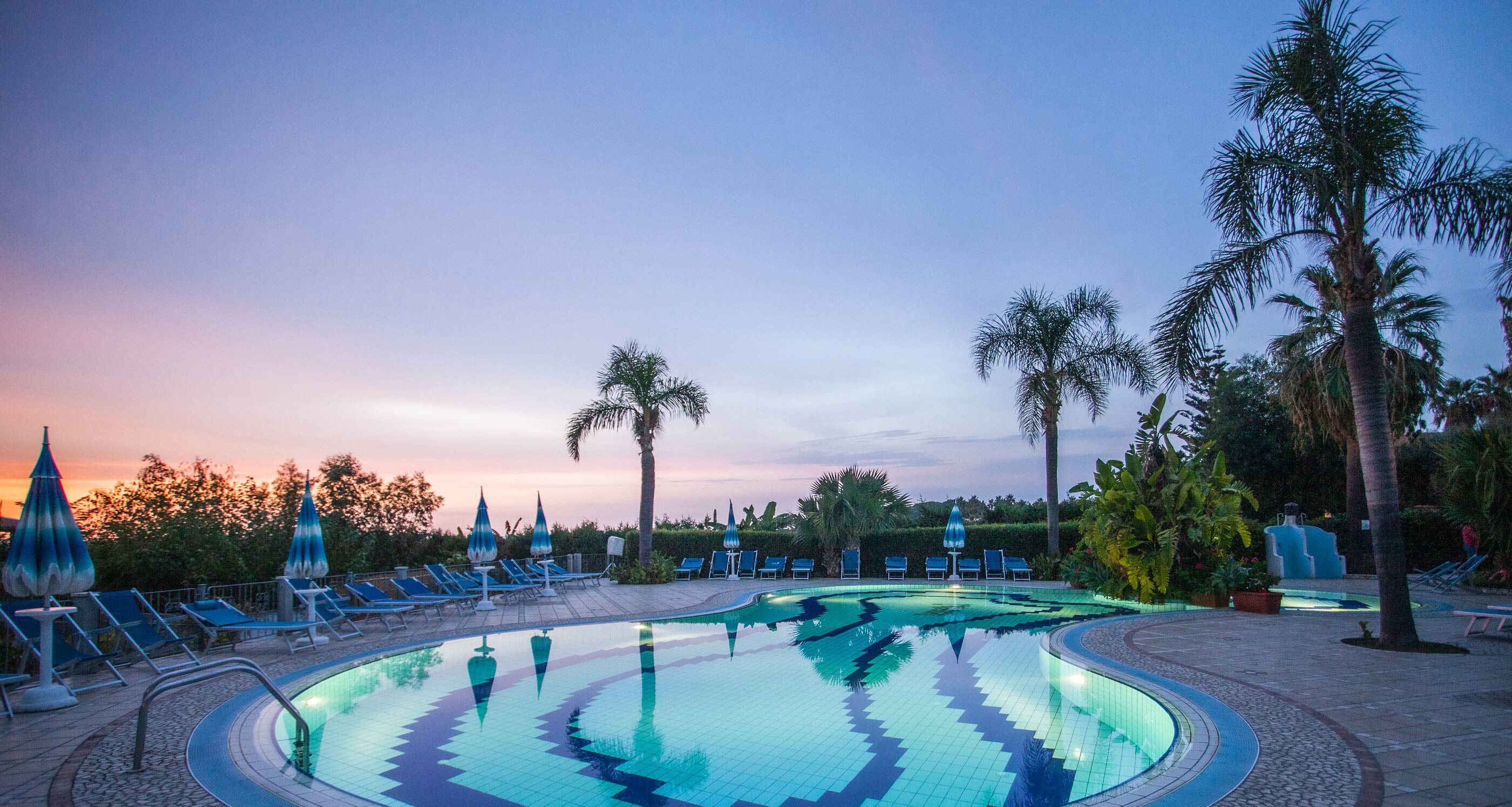 Una piscina con sillas de descanso y palmeras, rodeada de un jardín ajardinado.
