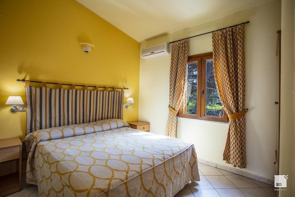 Une chambre avec un lit, deux lampes de chevet, une fenêtre avec des rideaux et un appareil de climatisation.