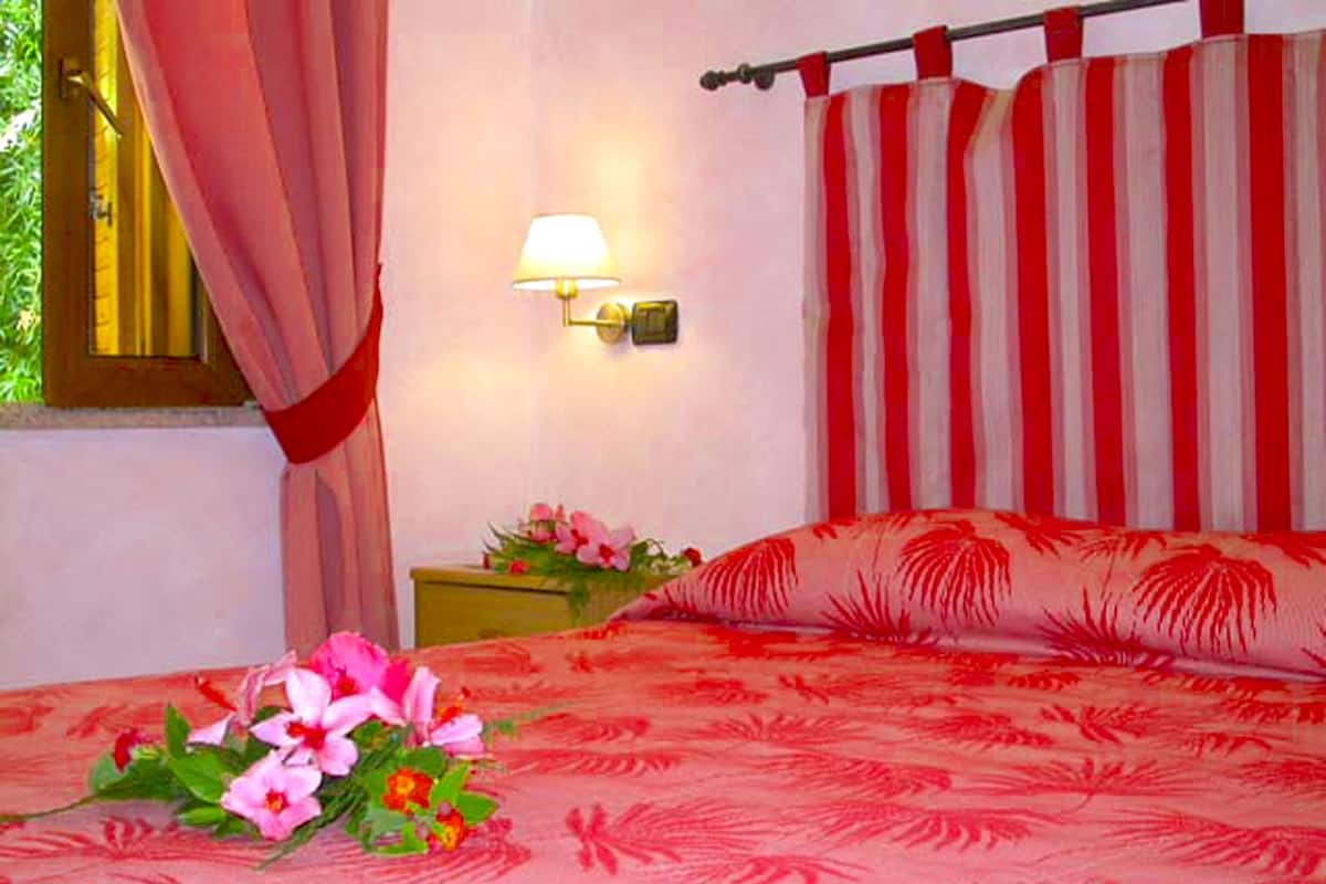 A hotel room with a bed, a nightstand, a lamp, and a window with curtains.