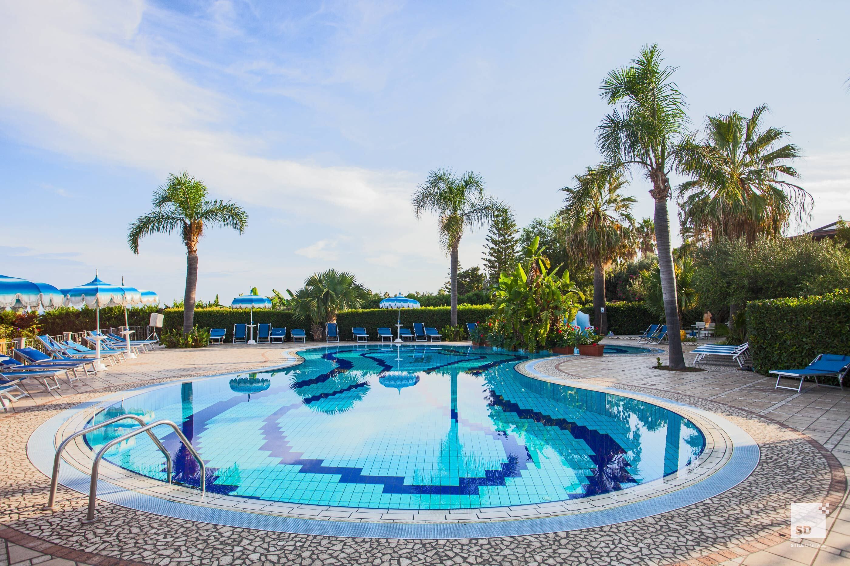 Ein Swimmingpool mit blauen Fliesen, umgeben von Liegestühlen und Palmen.