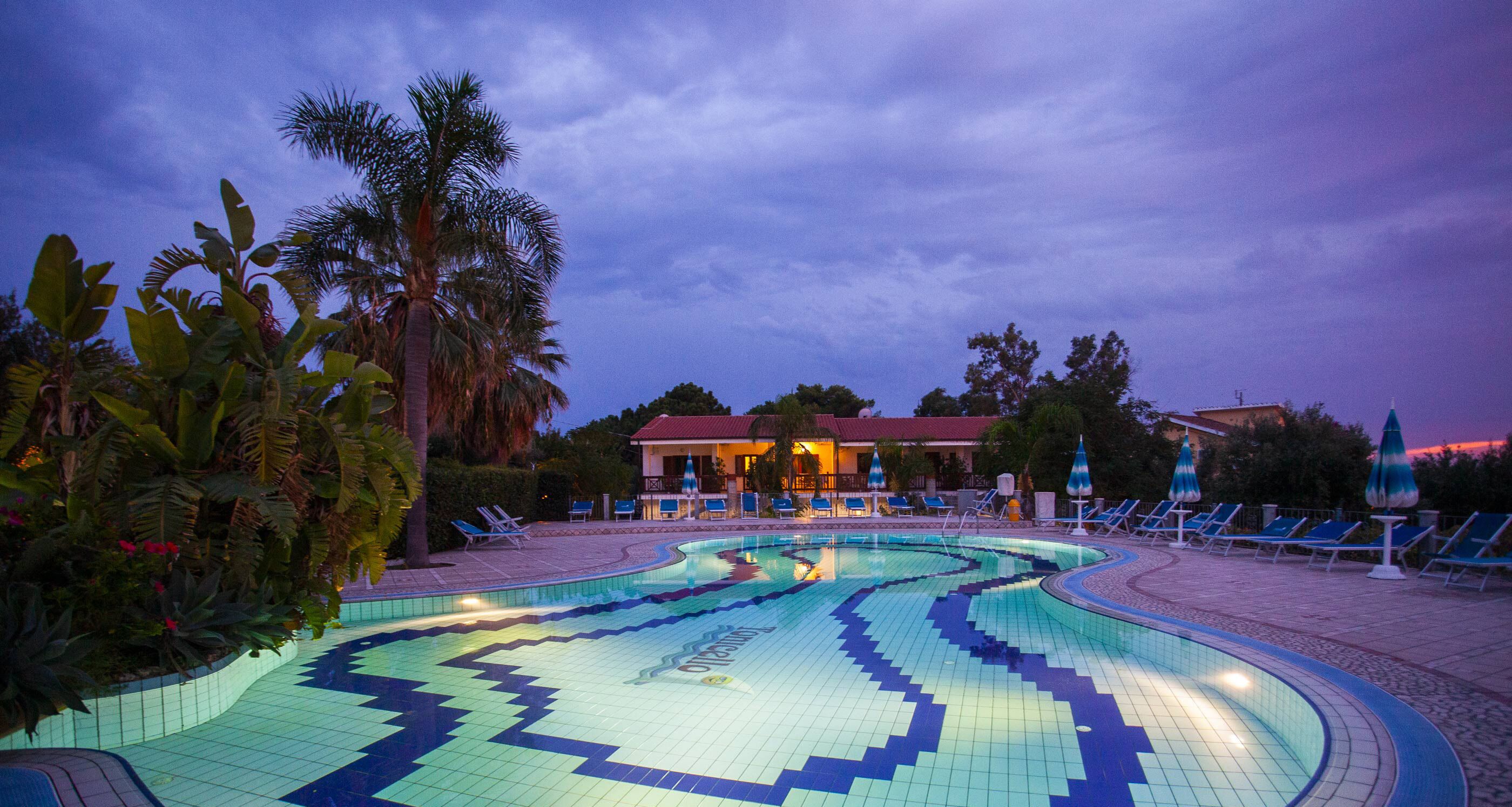 A swimming pool with a geometric tile pattern, surrounded by palm trees and lounge chairs.