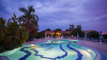 A swimming pool with a geometric tile pattern, surrounded by palm trees and lounge chairs.