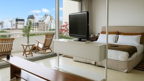 Hotelkamer met een bed, een bureau, een stoel, een televisie en een balkon met uitzicht op de stad.