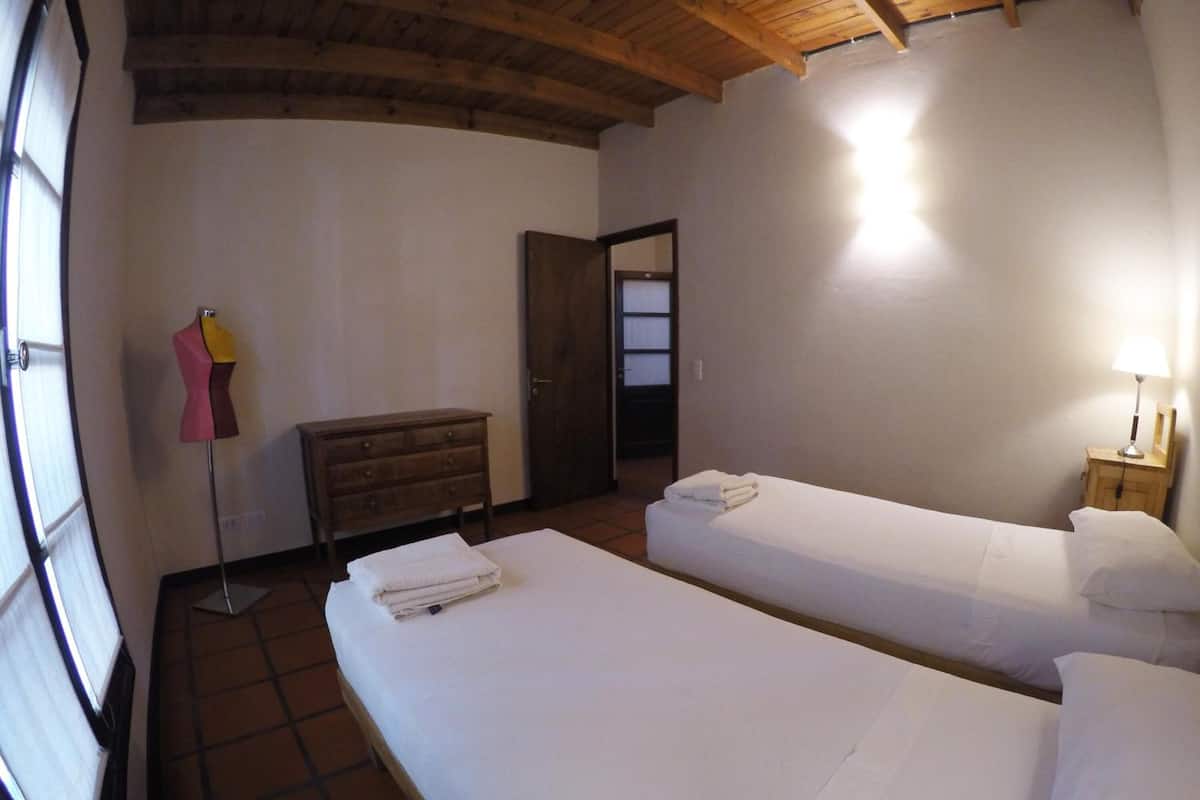 A room with two single beds, a wooden dresser, a mannequin, and a door leading to another room.