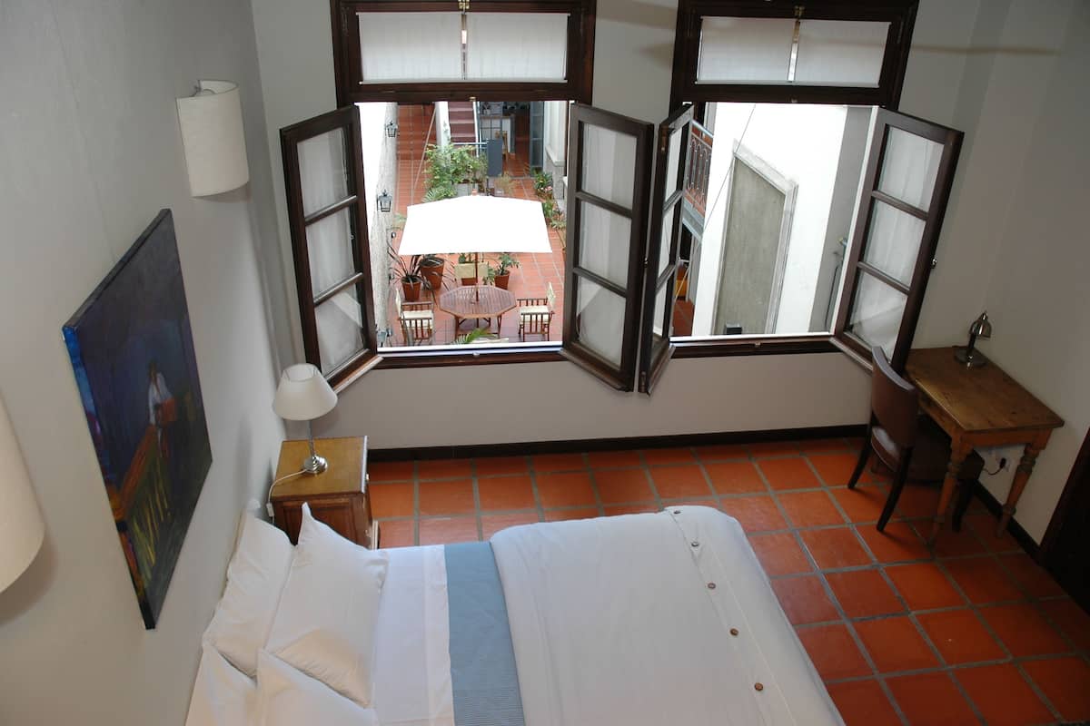 A hotel room with a bed, a desk, and a view of an outdoor patio through open windows.