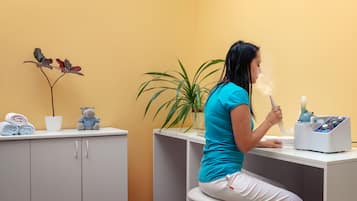 A person sitting at a desk with a medical device, a plant, and folded towels on a counter.