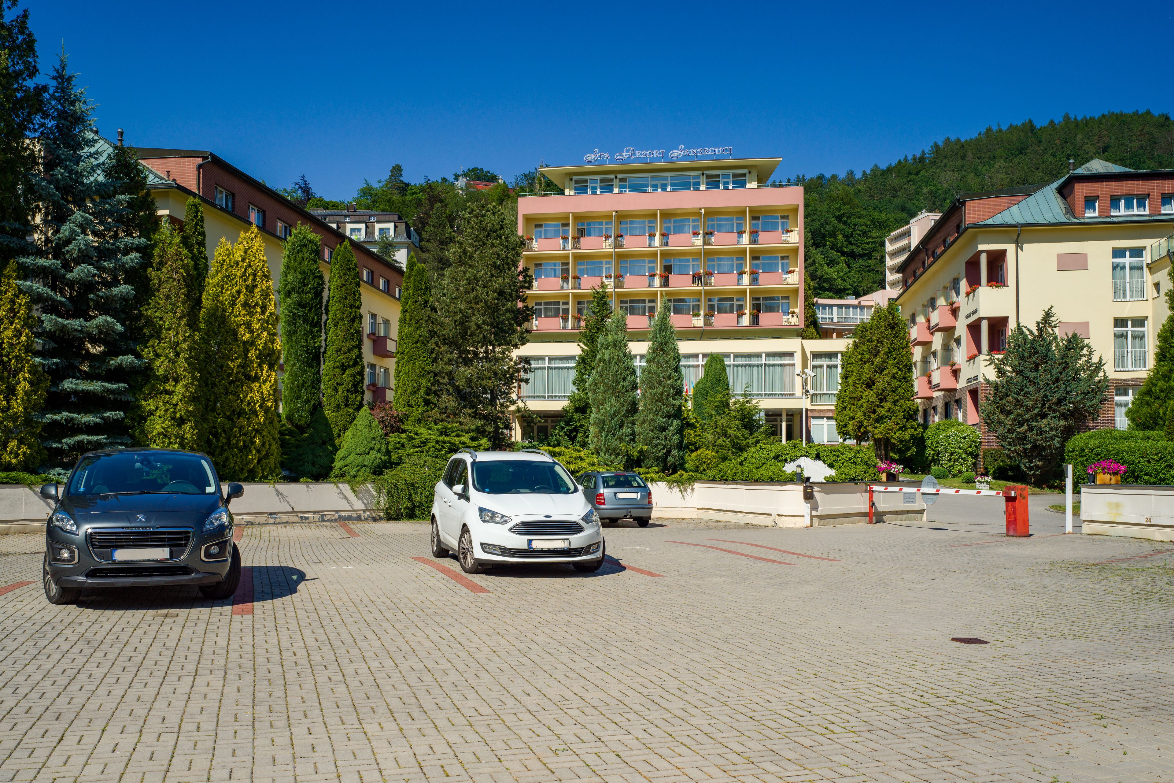 Een hotel met meerdere verdiepingen, een centraal atrium, een parkeerplaats en omliggend groen.