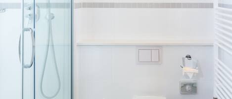 Un baño moderno con ducha de vidrio, inodoro blanco y un cesto de basura.