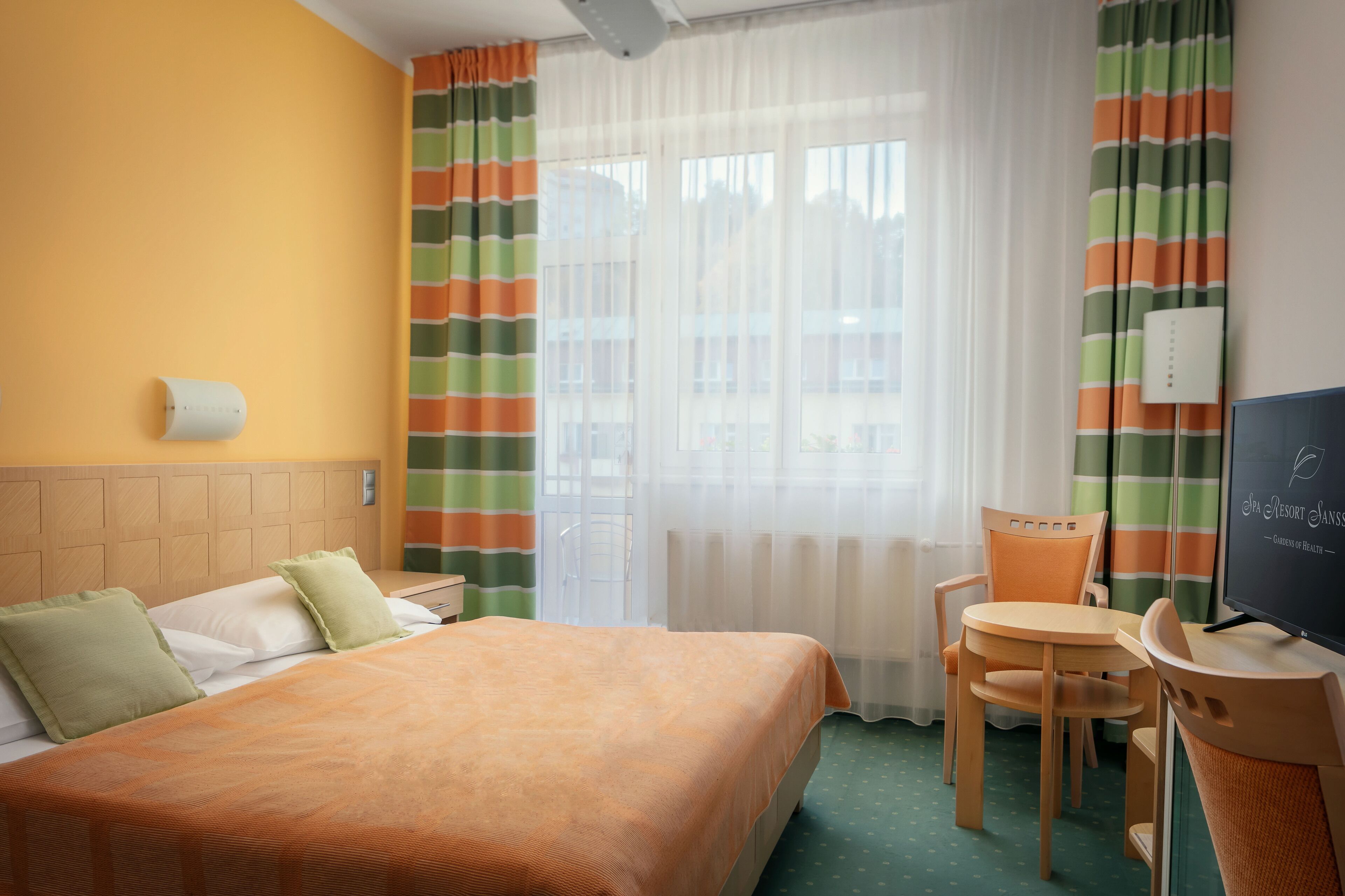 Una habitación de hotel con cama, escritorio, silla, televisión y cortinas.