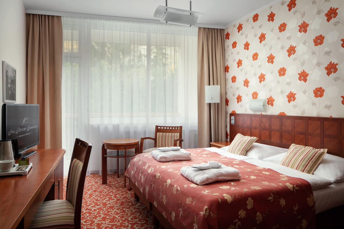 Ein Hotelzimmer mit Bett, Schreibtisch mit Fernseher, Sessel und einem Fenster mit Vorhängen.