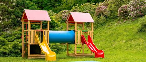 Un parque infantil con dos casitas, toboganes y un tapete verde sobre el césped.