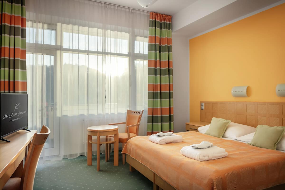 Ein Hotelzimmer mit Bett, Schreibtisch, Stuhl, Fernseher und einem Fenster mit Vorhängen.