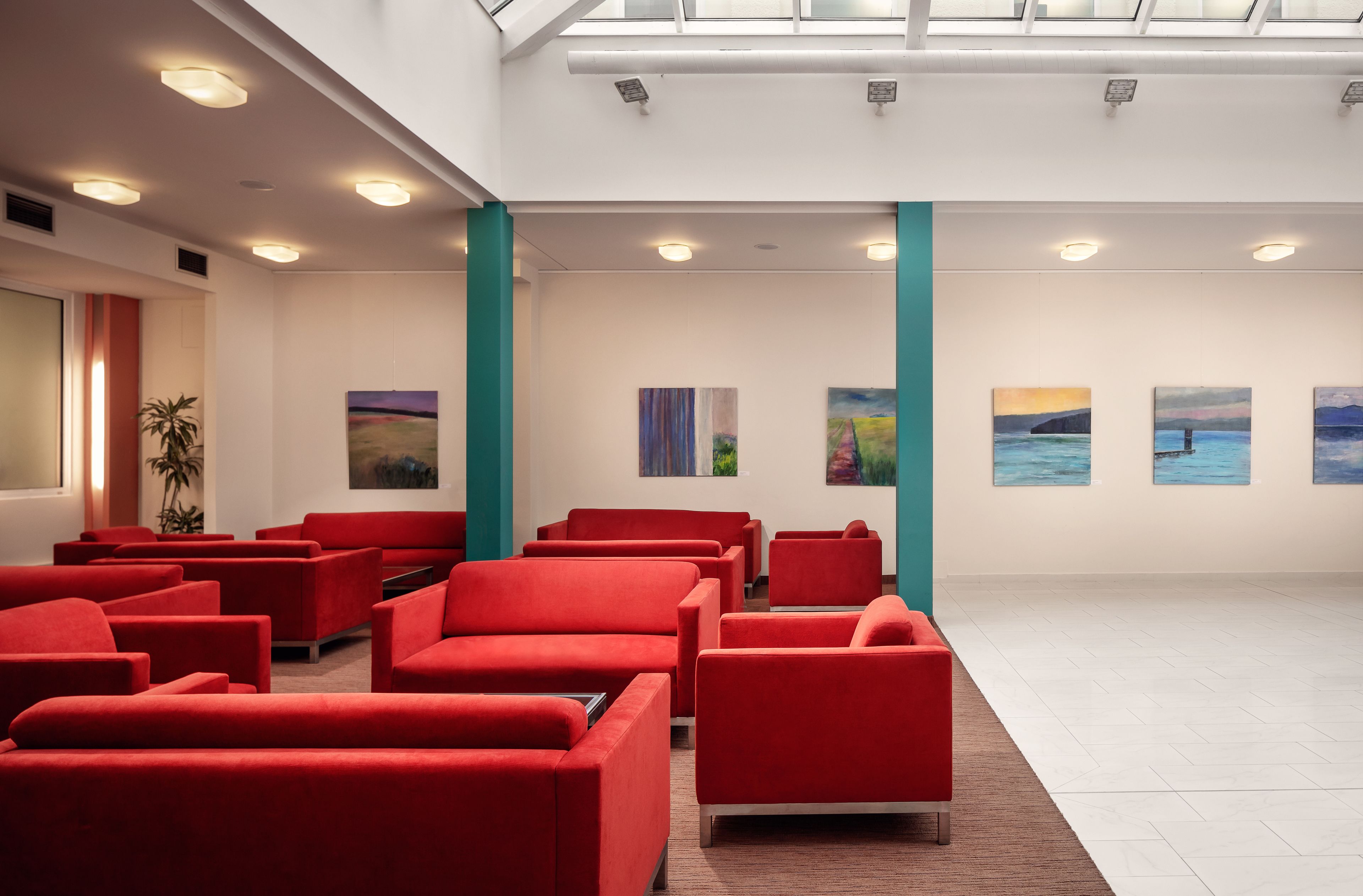 A modern lobby with red seating, artwork on the walls, and a skylight.