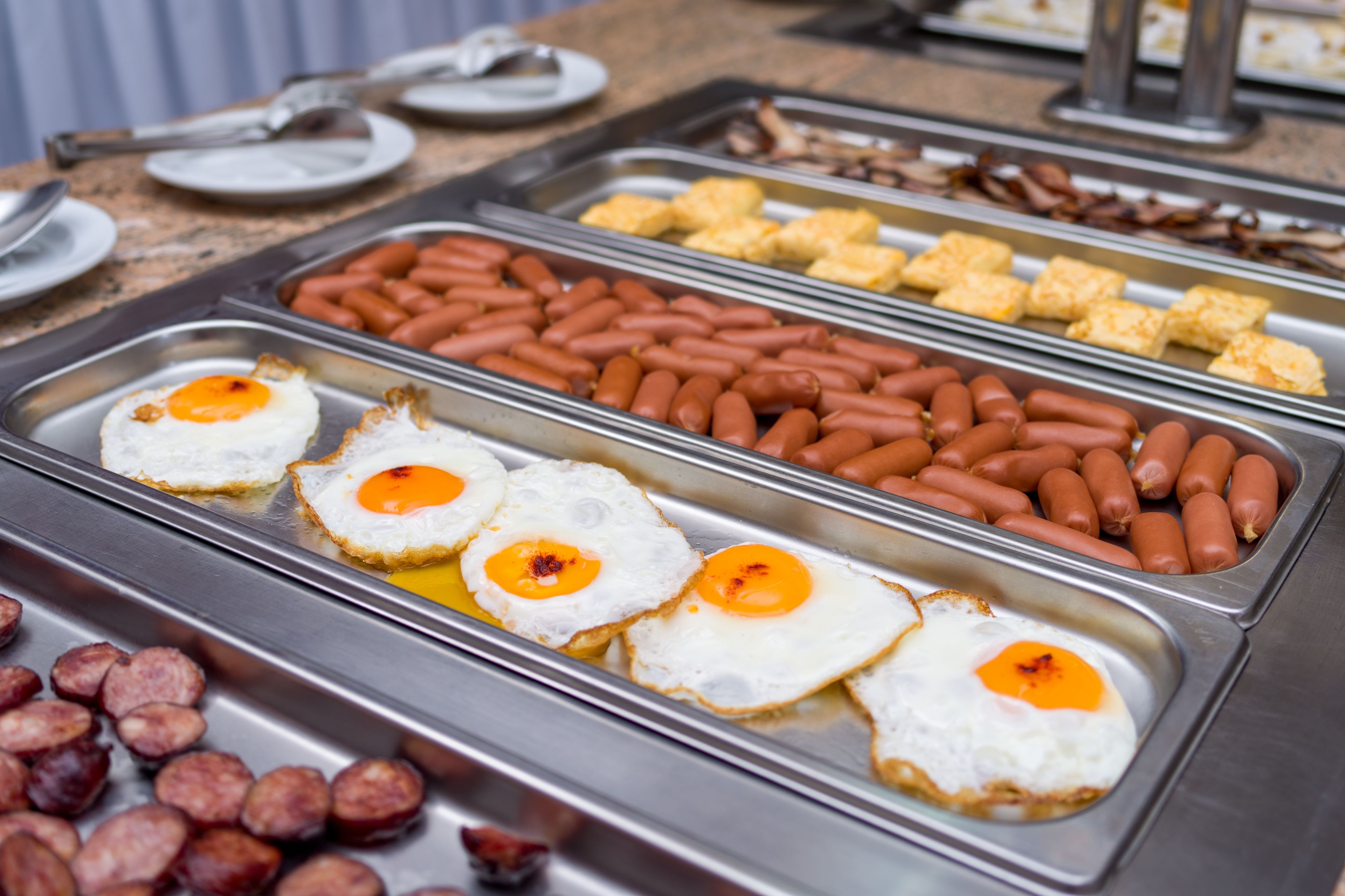 Un bufé con diversas opciones de desayuno, como huevos, salchichas y pasteles.