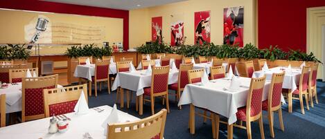 A conference room with multiple tables and chairs, white tablecloths, and red chairs.