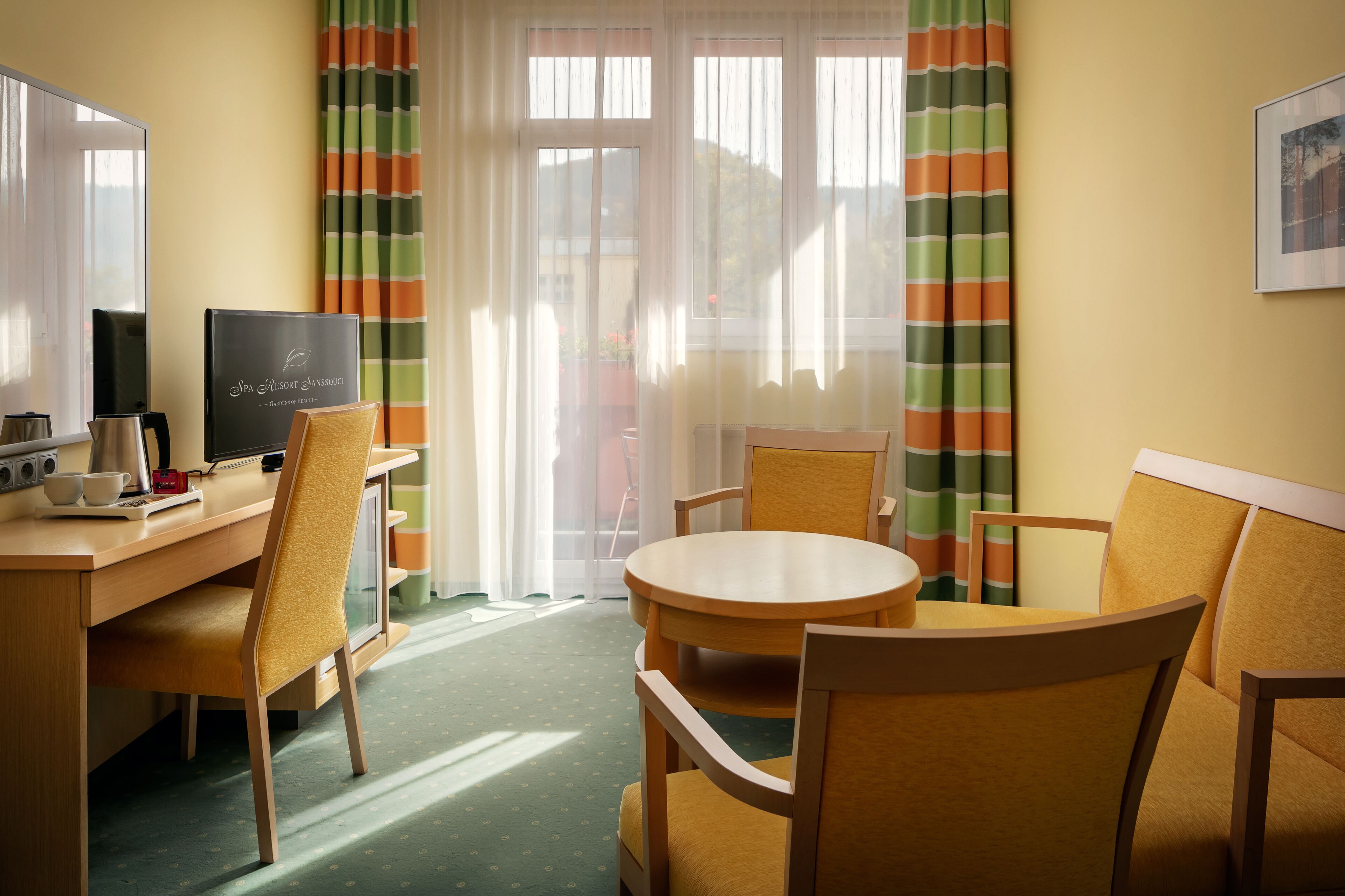 A hotel room with a desk, chairs, a round table, a TV, and a window with curtains.