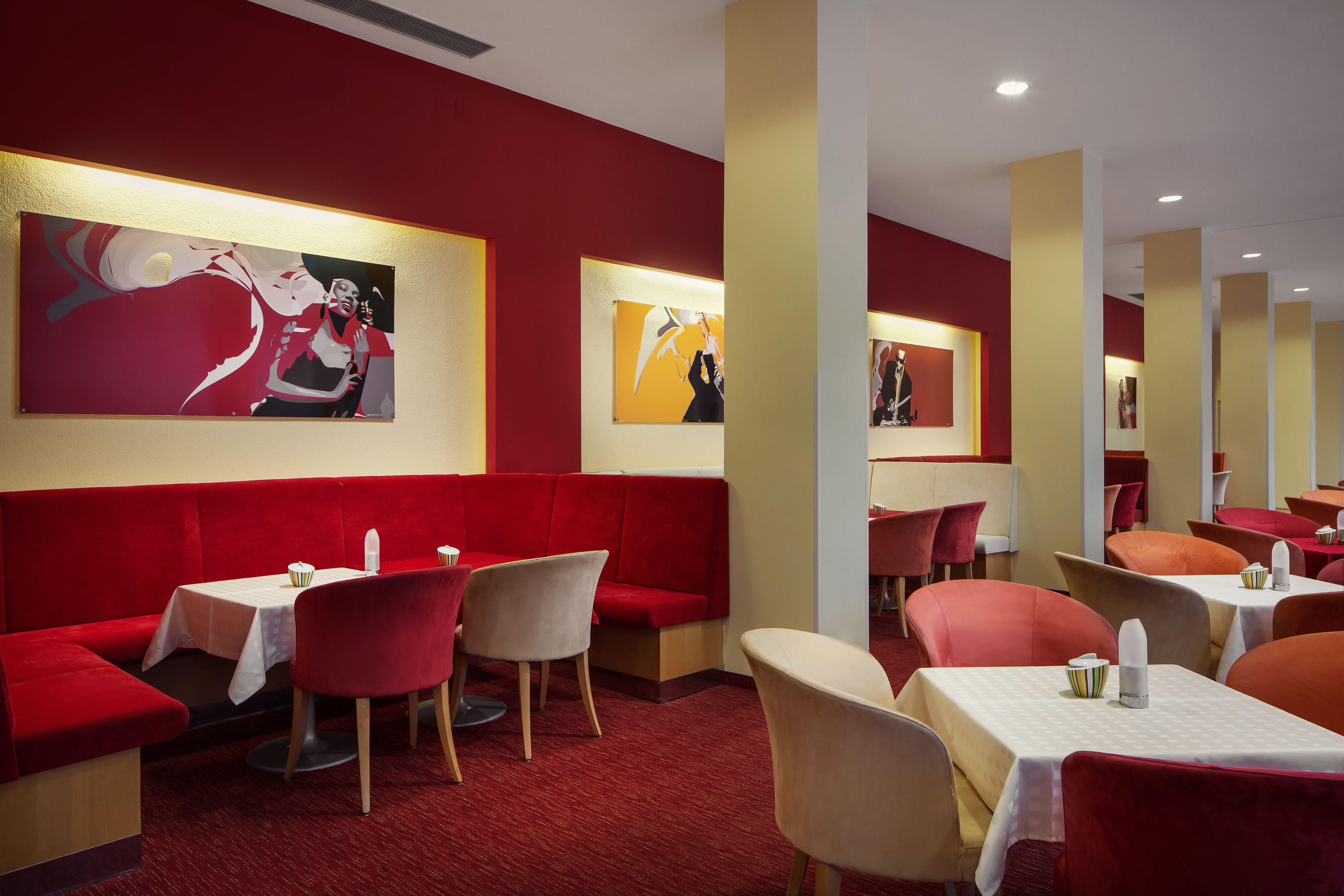 A restaurant with red booths and tables, featuring artwork on the walls.