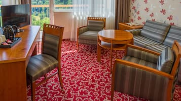 Een hotelkamer met een rood kamerkleed, een bank, twee fauteuils, een klein rond tafeltje en een televisie op een houten dressoir.