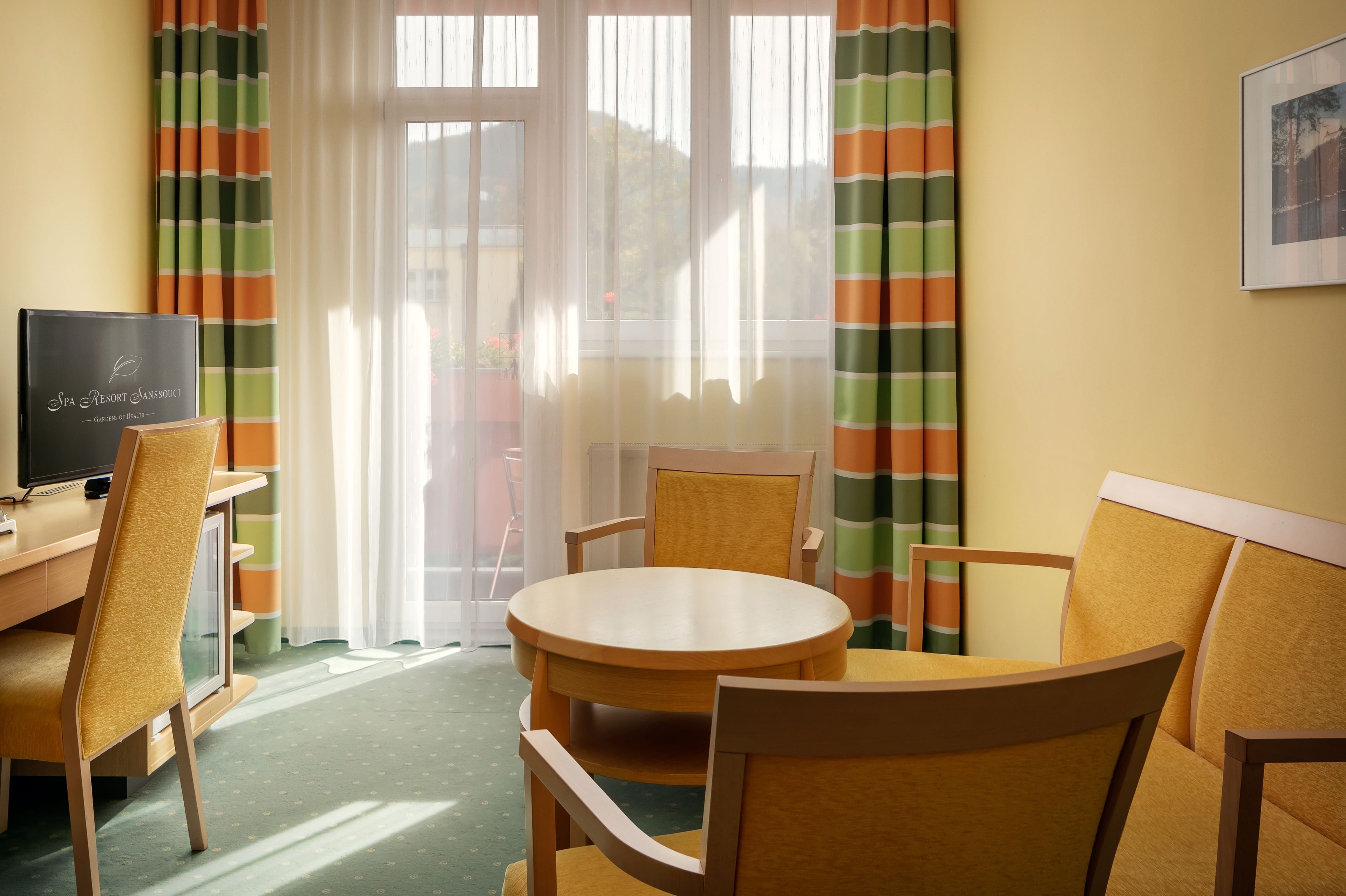 Ett hotellrum med ett runt träbord, två stolar, en tv och ett fönster med gardiner.