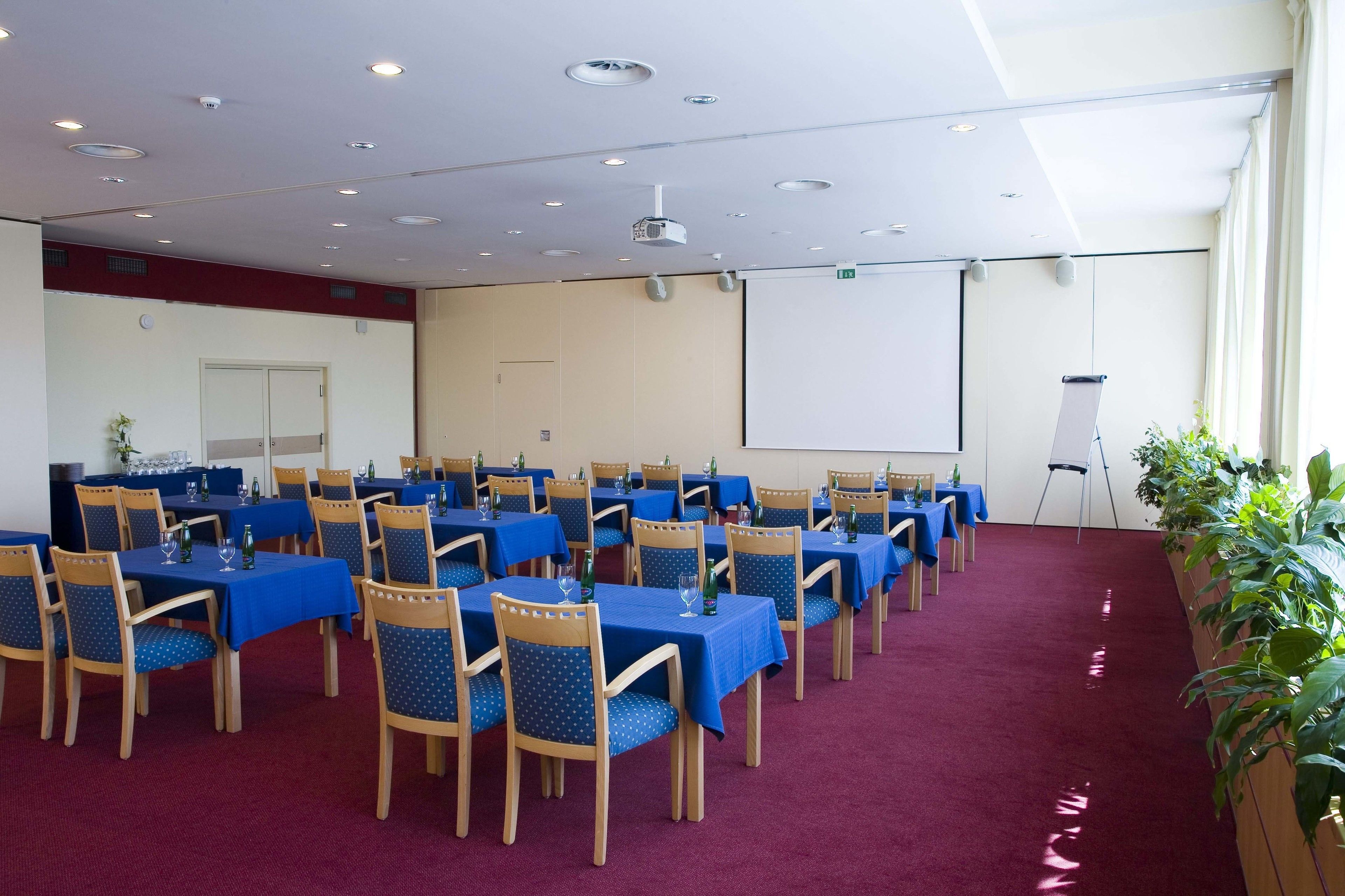 A conference room with rows of tables and chairs, a projector screen, and a large window.