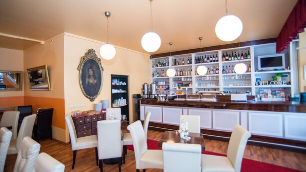 Un espace bar avec un comptoir en bois, des chaises blanches et une variété de bouteilles et de verres disposés sur des étagères.