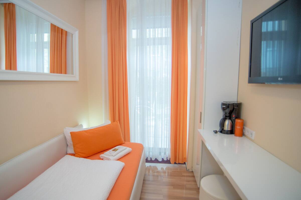 Una habitación de hotel con cama, una mesita con cafetera y un televisor en la pared.