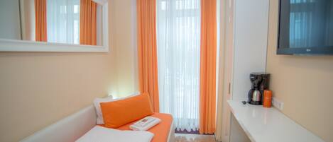 A hotel room with a bed, a small table with a coffee maker, and a TV on the wall.