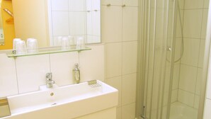 Une salle de bain avec un lavabo blanc, un miroir et une douche en verre.